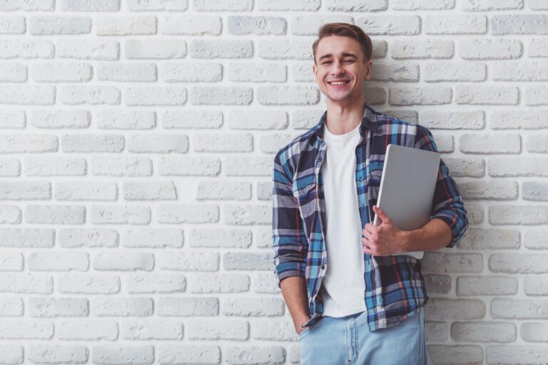 leanerner standing against a wall holding a laptop